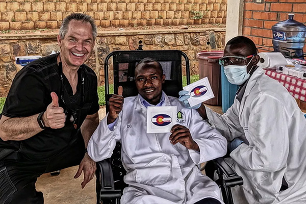 The image shows three individuals posing with a cardboard cutout of a person wearing a white lab coat, which suggests a medical or scientific context.
