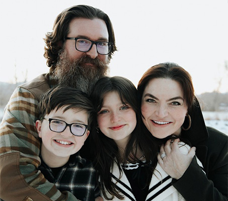 A family photo with a man, woman, and two children smiling at the camera, taken during wintertime outdoors.