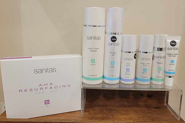 The image shows a collection of skincare products on display, including a boxed set with visible branding, placed next to a glass shelf containing additional items, all arranged on a surface.